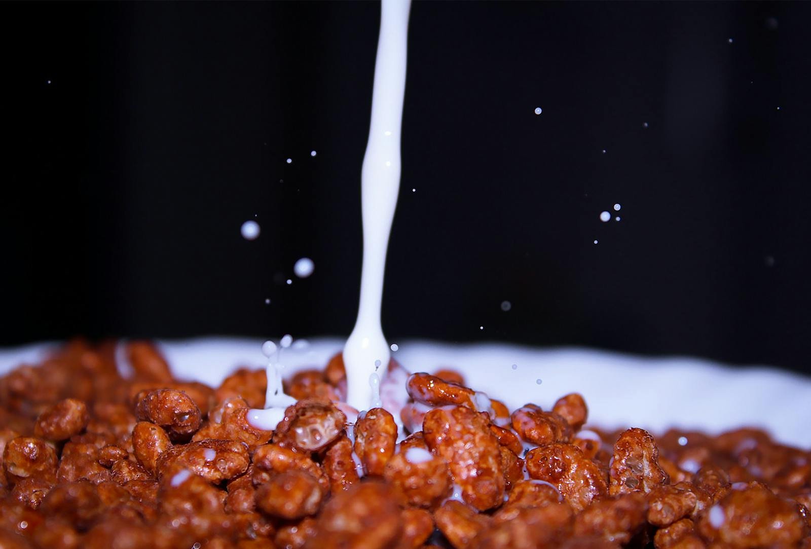 Milk splashes onto chocolate cereal, capturing a dynamic breakfast moment.